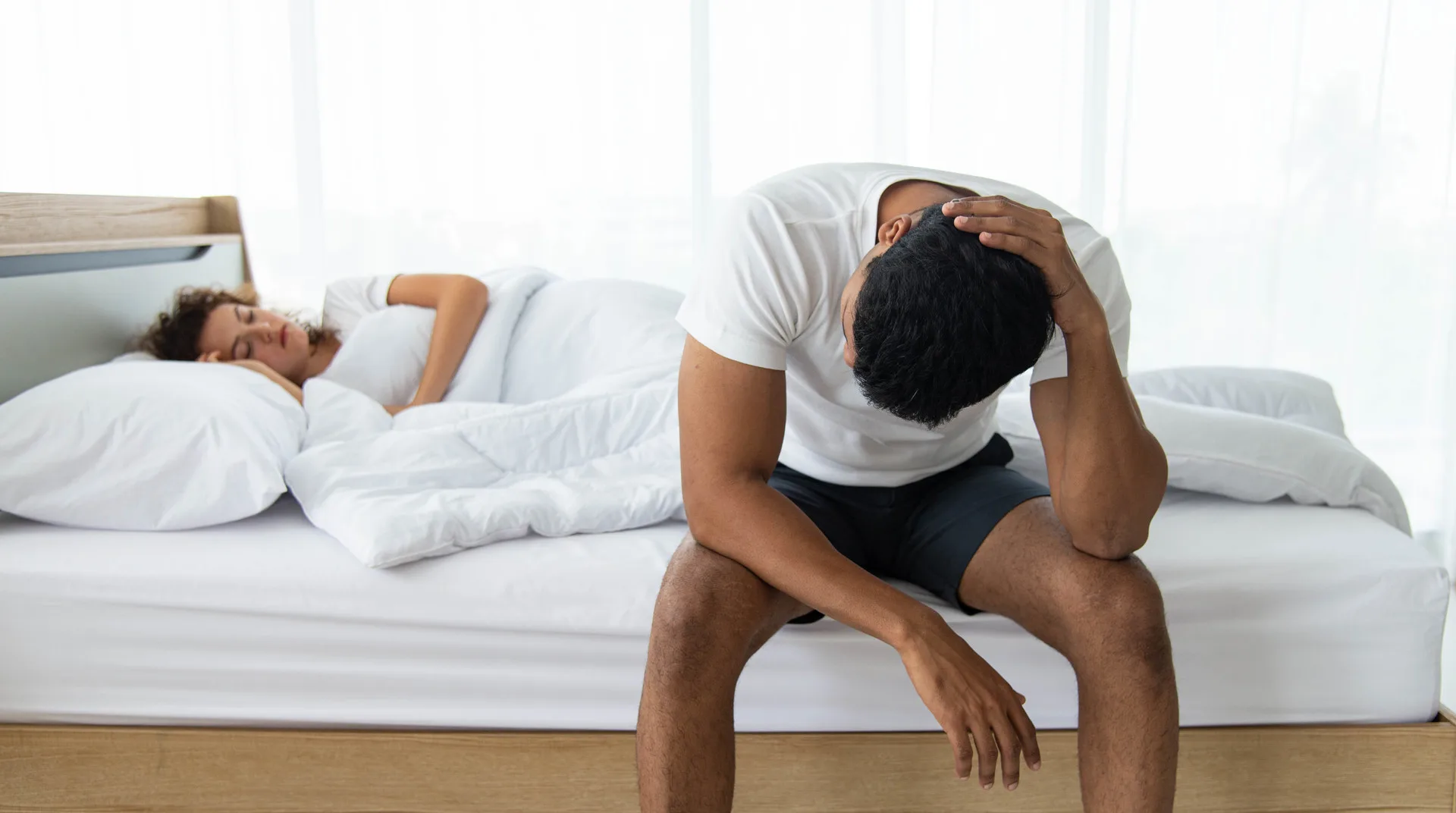 Man sitting on the edge of the bed with his head down, worried about erection problems that natural support can help with