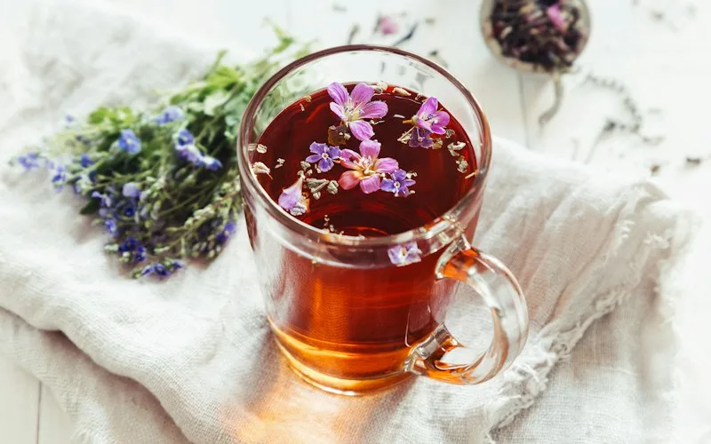 Glass mug of herbal tea beside fresh lavender and flowers, representing natural, naturopathic support for low libido