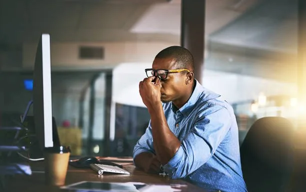 Stressed man rubbing his eyes at his desk late at night, a common trigger for erection problems that natural support can help with
